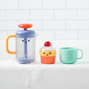 Colorful bath toy set including a bubble pump, smiling cupcake, and a green cup, all on a white surface with bubbles.