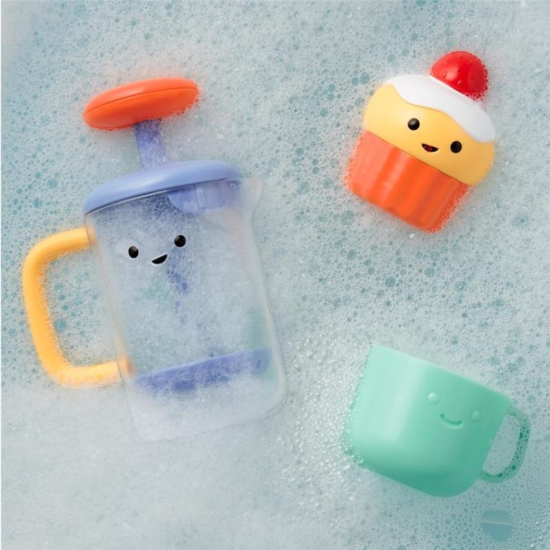 Colorful bath toys including a cup with a smiling face, a bubble frother, and a cupcake, floating in soapy water.