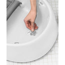 Hand adjusting the gray flower-shaped stopper in the bottom of the Skip Hop Moby Baby Bath Tub, which is white and designed for infants.