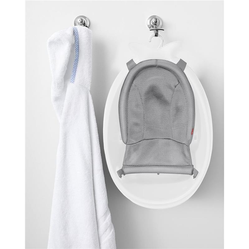 Baby bath tub with a gray mesh sling hanging on a wall, alongside a white hooded towel.