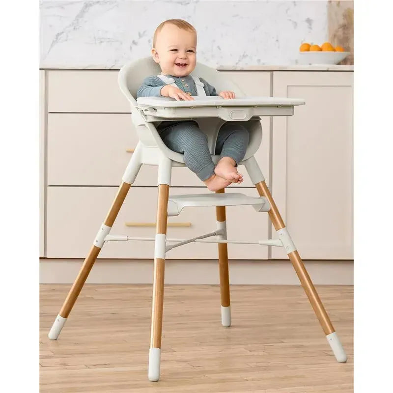 Skip Hop EON 4-in-1 High Chair in Oat, featuring a smiling baby in a gray outfit, sitting comfortably with bare feet and a tray.