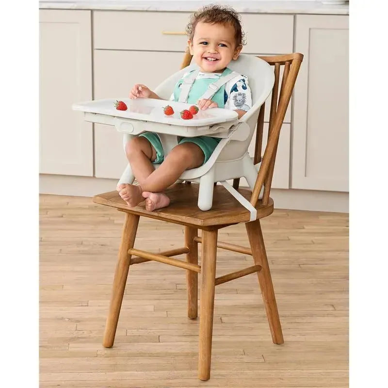 Skip Hop EON 4-in-1 High Chair in Oat with a smiling child sitting on a wooden chair, featuring a removable tray with strawberries.