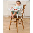 Skip Hop EON 4-in-1 High Chair in Oat with a smiling child sitting on a wooden chair, featuring a removable tray with strawberries.