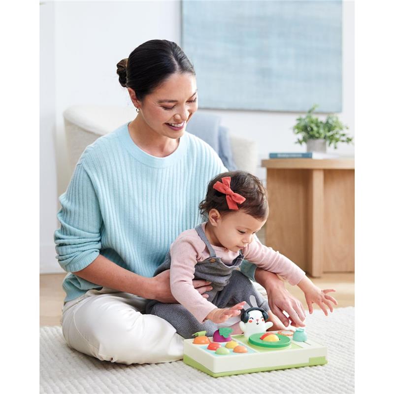 A woman sits with a toddler playing with the Skip Hop Baby Musical DJ Set Toy featuring colorful lights and sound effects.