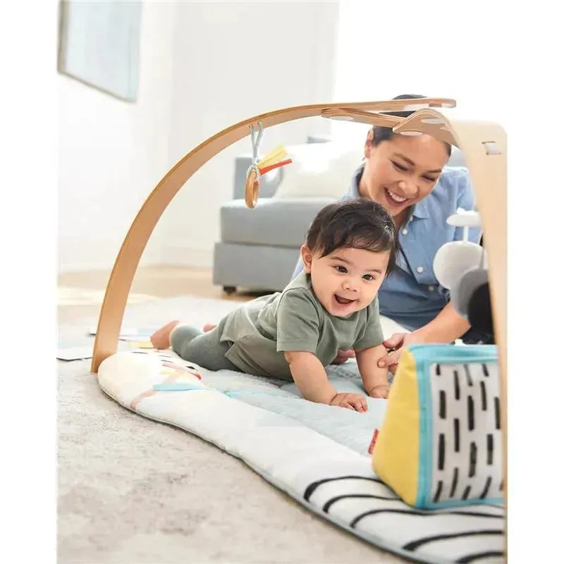 Montessori-inspired baby play gym with a smiling infant on the playmat, reaching towards colorful toys while an adult observes.