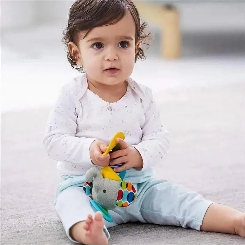 Toddler sitting on the floor, holding a yellow teether while playing with the Skip Hop Elephant toy featuring colorful patterns.