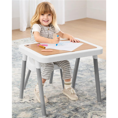 A child with long hair smiles while drawing on paper at the Skip Hop Discoverosity Wood Table Top for 3-in-1 Sensory Table.