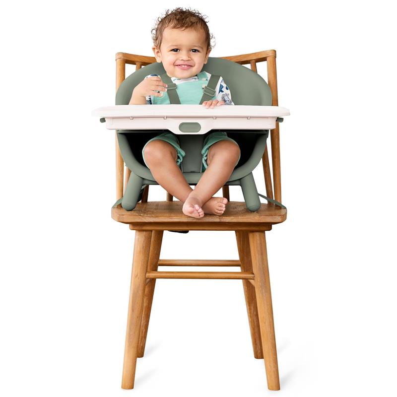 High chair with a smiling baby in a green seat, featuring a white tray, placed on a wooden chair.