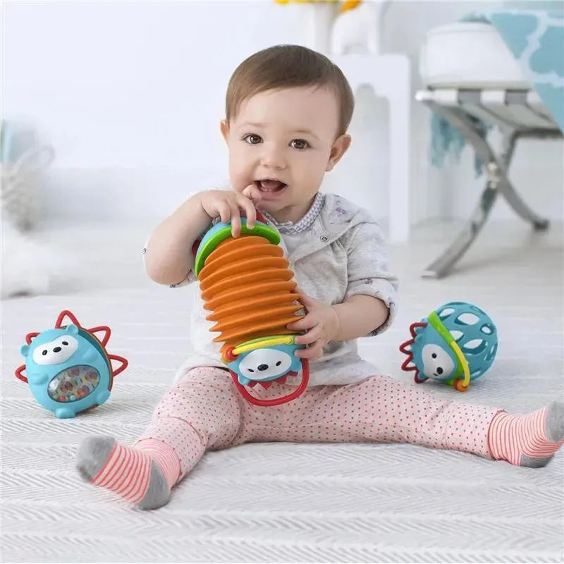 Toddler playing with the Skip Hop Explore & More Hedgehog Accordion toy and two colorful balls on a textured floor.
