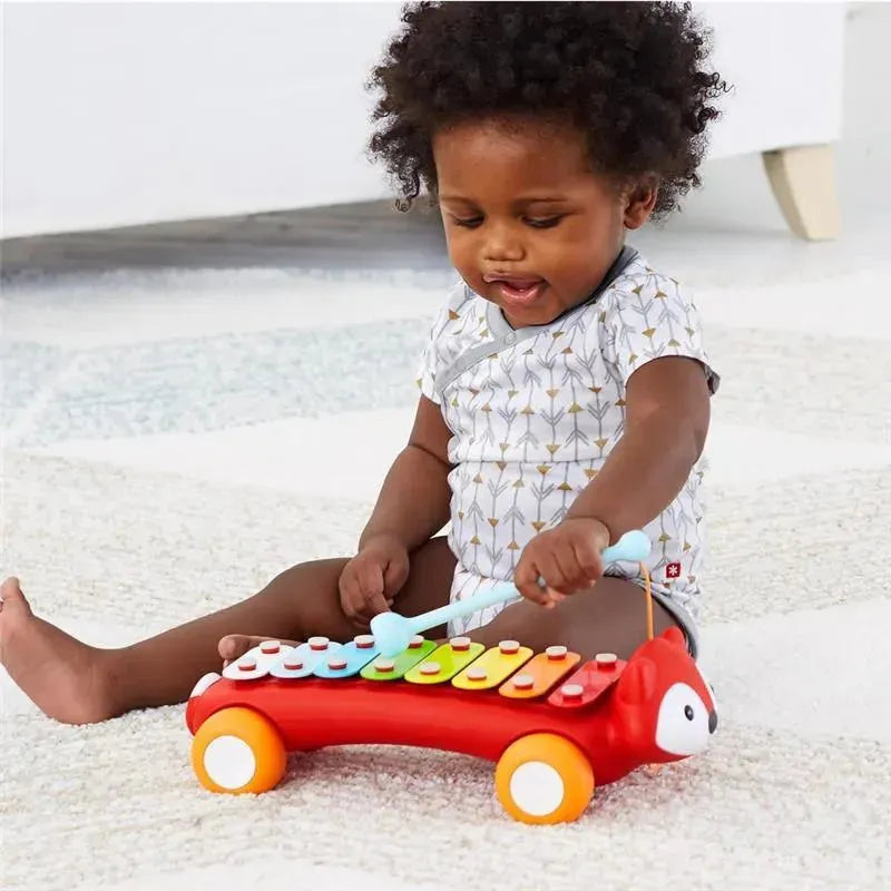 Toddler playing with the Skip Hop Explore & More Musical Toy Xylophone, shaped like a fox, on a carpeted floor.