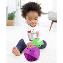 A toddler sits on a carpet, playing with a purple beet-shaped toy with green leaves and a smiling face.
