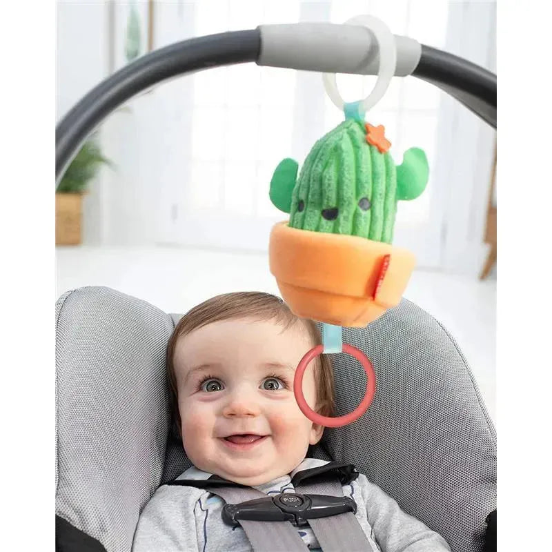 Cactus Jitter Hanging Toy by Skip Hop is attached to a baby car seat, with a smiling baby in the foreground.