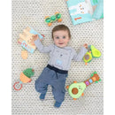 Baby lying on a textured blanket surrounded by toys, including the Skip Hop Cactus Jitter Hanging Toy, with a joyful expression.