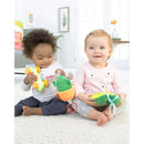 Two babies sit on a soft surface, one holding a cactus-shaped toy with a ring and the other a green wheeled toy, both smiling.