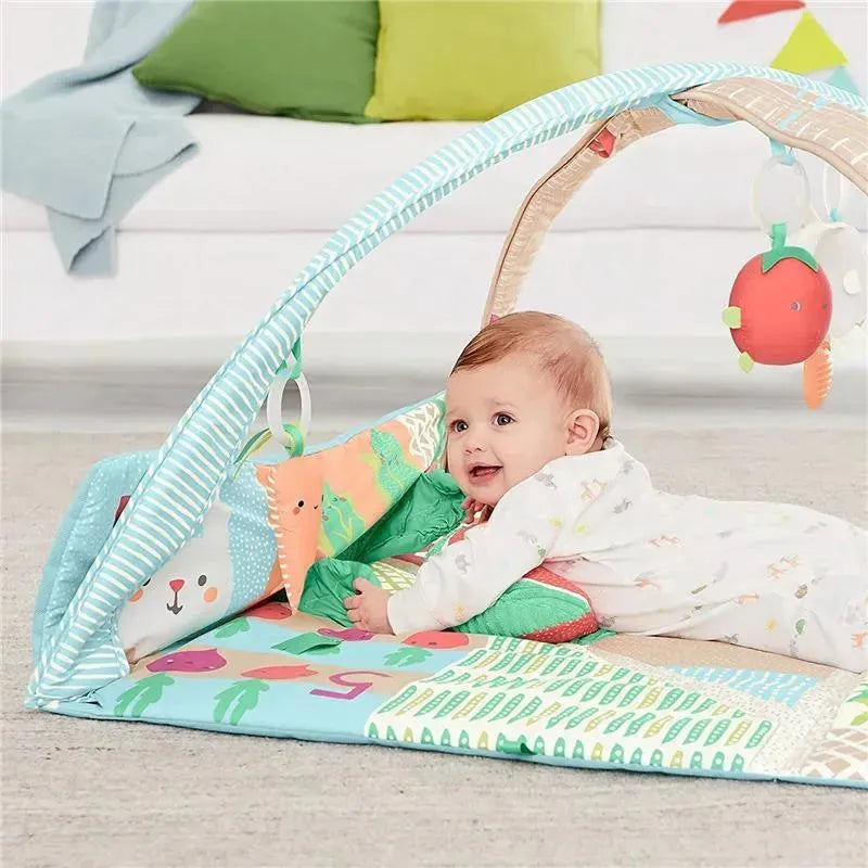 Baby playing on the Skip Hop Farmstand Activity Gym, surrounded by colorful cushions and hanging toys in a vibrant garden theme.