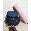 Navy Skip Hop Forma diaper bag backpack with quilted pattern, two zippers, and tan accents, alongside a pink yoga mat and black shoes.