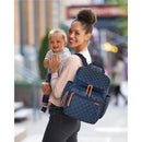 A smiling woman holds a baby while wearing a navy Skip Hop Forma Diaper Bag Backpack with quilted design.