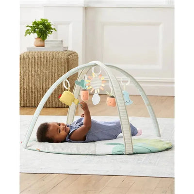 Skip Hop Garden Oasis Activity Gym with a baby lying on a soft mat, reaching for hanging toys including a watering can and other colorful shapes.