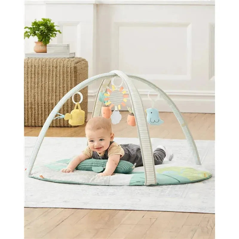 Baby playing on a Skip Hop Garden Oasis Activity Gym with hanging toys, surrounded by a soft mat.