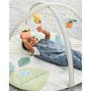 Baby playing on a floral-patterned mat under a curved activity gym with hanging toys, including a smiling plant pot.