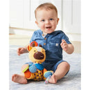 Toddler sitting on a rug with a Skip Hop Bandana Buddies Giraffe stroller toy, smiling and reaching for the toy.