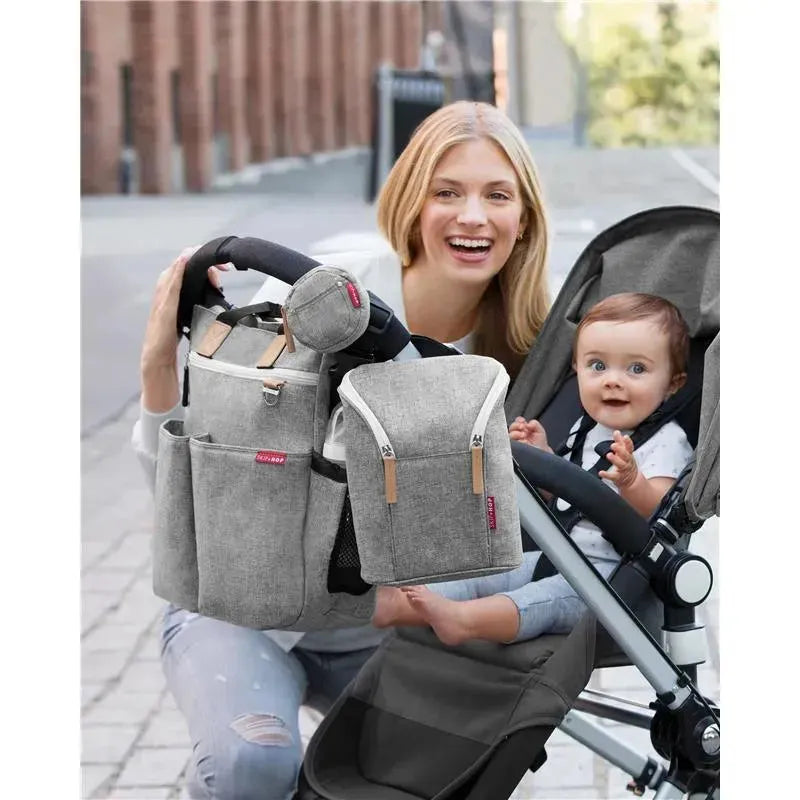 Grey melange Skip Hop Grab & Go Double Bottle Bag attached to a stroller, with a woman smiling beside a baby.