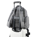Heather grey Skip Hop Luna Diaper Bag Backpack positioned on a white suitcase, showcasing its adjustable straps and side pocket.