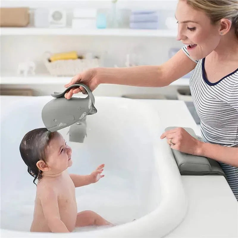 A mother joyfully bathes her baby in a bathtub using a grey whale-shaped watering can from the Skip Hop Moby Baby Bath set.