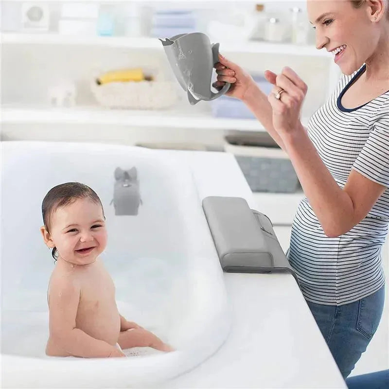 A smiling baby sits in a bath, while a woman holds a grey whale-shaped bath pourer, enjoying the bath time together.