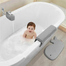 Baby sitting in a white bathtub filled with bubbles, smiling, with a grey whale-shaped faucet cover and a bath mat nearby.