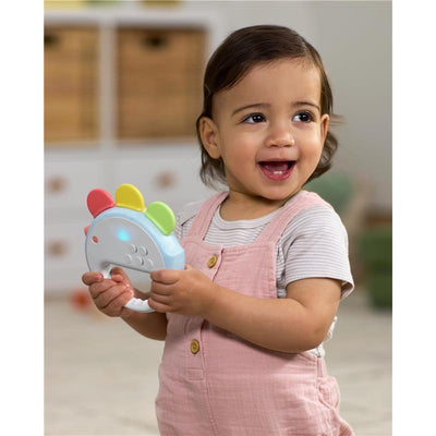 Happy toddler holds a Skip Hop musical toy with colorful buttons, featuring lights and sounds, in a playroom setting.