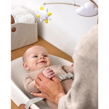 Baby lying on a Skip Hop wipe-clean changing pad, smiling at a mobile with a star, while an adult gently holds their hand.