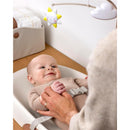 Baby lying on a Skip Hop wipe-clean changing pad, smiling at a mobile with a star, while an adult gently holds their hand.