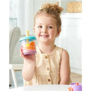 Young child smiling while holding a transparent smoothie cup filled with colorful toy fruits, showcasing the Skip Hop Narwhal Smoothie Set.