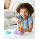 A young girl smiles while using the Skip Hop Narwhal Smoothie Set, stirring colorful play food in a cup.