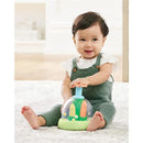 Baby sitting on a soft surface, smiling while playing with the Skip Hop Farmstand Push and Spin toy featuring colorful vegetables.