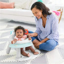 A baby with curly hair sits in a Skip Hop Silver Lining Cloud 2-in-1 Activity Floor Seat with a smiling woman beside them.