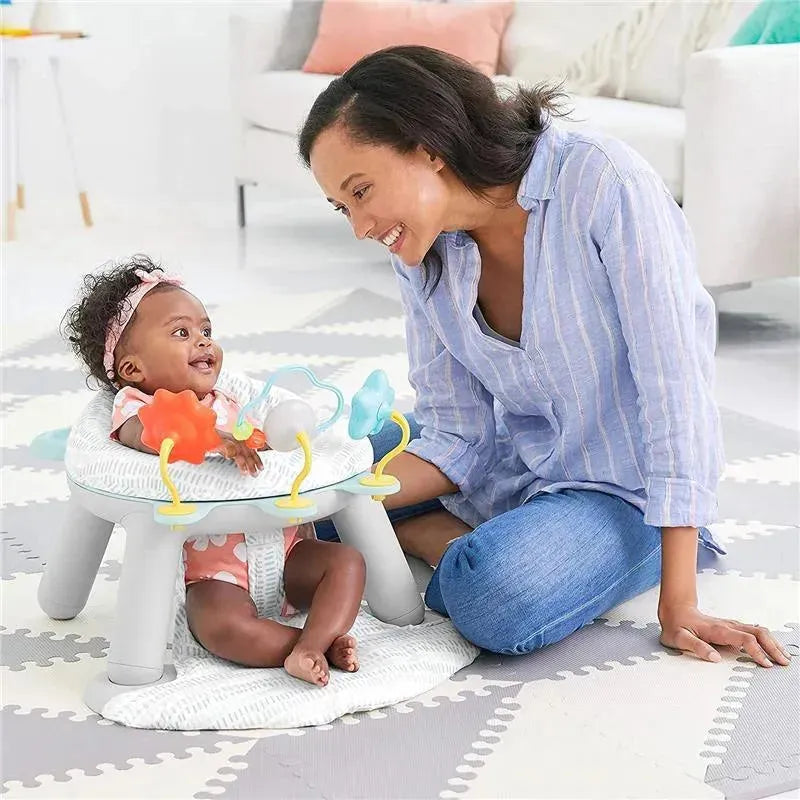 A baby sits in a Skip Hop Silver Lining Cloud 2-in-1 Activity Floor Seat, smiling at a woman leaning close, engaged in play.