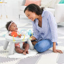 A baby sits in a Skip Hop Silver Lining Cloud 2-in-1 Activity Floor Seat, smiling at a woman leaning close, engaged in play.