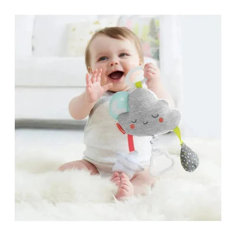 Baby happily holding the Skip Hop Silver Lining Cloud Jitter Stroller Toy with colorful features on a soft rug.