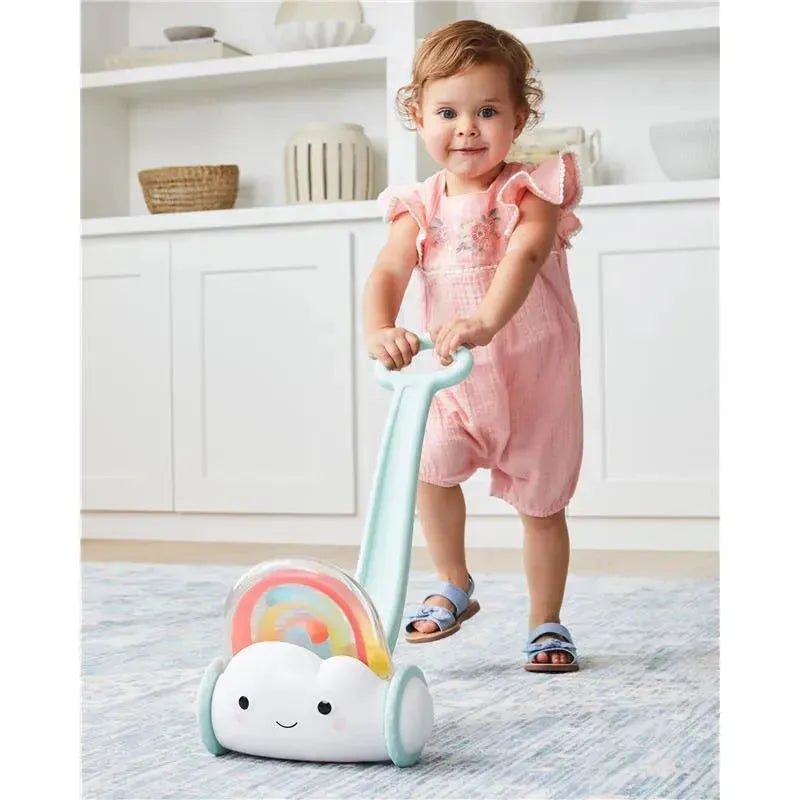 Toddler in a pink outfit pushes a Skip Hop Silver Lining Cloud Push Toy with a rainbow design.