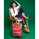 Big kid wearing glasses sits on a chair, smiling beside a red strawberry-themed backpack with a green top.