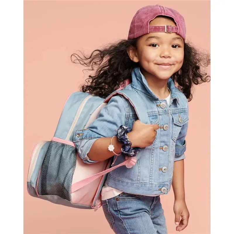 Little girl wearing a denim jacket and cap, smiling while carrying a Skip Hop Spark Style Rainbow backpack.
