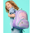 Little girl smiling while holding a seashell-themed purple backpack adorned with iridescent details.