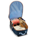 Blue Skip Hop Spark Style luggage, shaped like a rocketship, is open with packed clothes, sunglasses, and a hat inside.