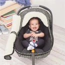 Grey feather-patterned car seat cover with a smiling baby inside, secured in a car seat with a soft lining.