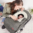 A woman gently holds a baby peeking out of a grey Skip Hop car seat cover with a feather pattern, featuring a soft white lining.