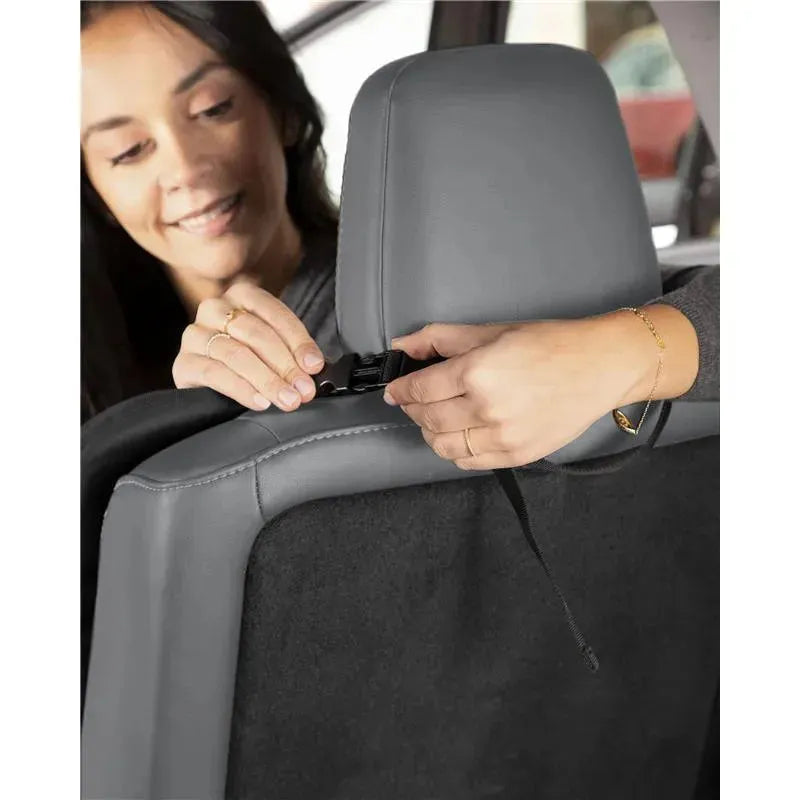 A woman attaches the Skip Hop Clean Child Car Seat Protector to a vehicle headrest, demonstrating its installation.