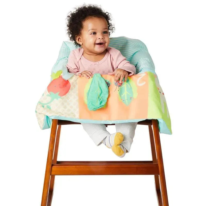Baby seated in a high chair with a colorful Skip Hop Farmstand Shopping Cart Cover featuring vegetable designs and textures.