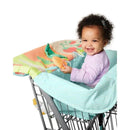 Baby sitting in a Skip Hop Farmstand Shopping Cart Cover, smiling while holding a teether toy, with colorful fabric visible.